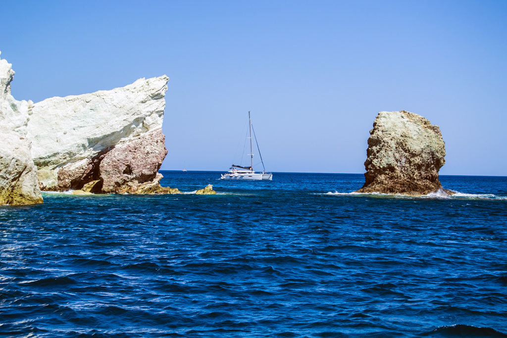 Barco entre grandes rocas de la playa blanca de Santorini - Descubrir Santorini